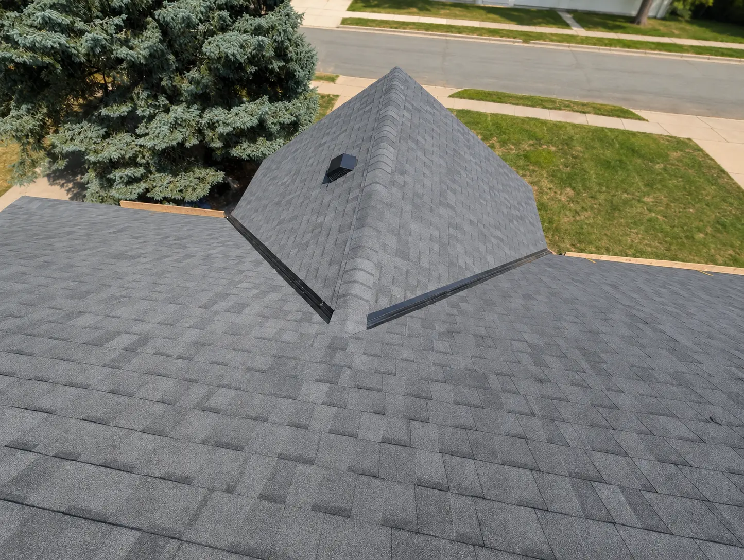 Aerial view of a finished hip roof in charcoal shingles with a ridge vent and box vent, new decking visible at the eaves.