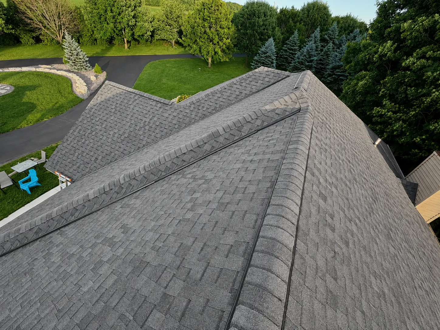Aerial view of a completed dark grey architectural shingle roof, with clean hip ridges and valleys running down to a wooded Wisconsin yard.