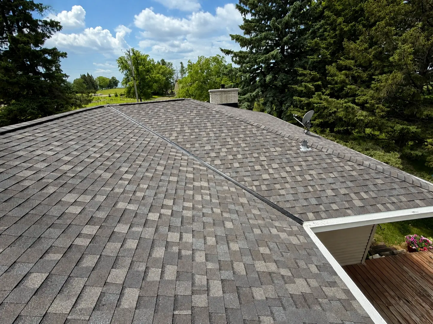 Wide shingle roof plane finished in weathered-wood coloured architectural shingles with farmland in the distance.